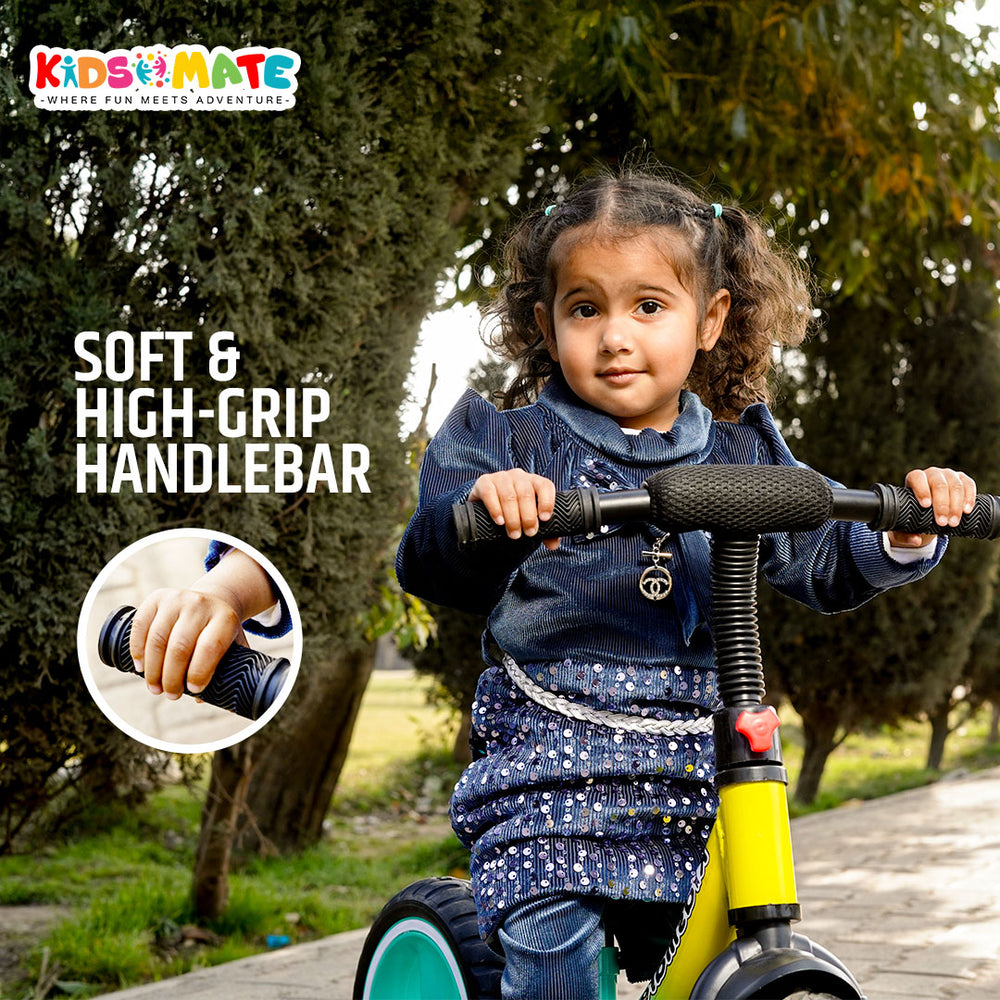 A child happily riding a colorful balance bike outdoors. The bike features a soft handlebar grip, and the Kidsmate logo is visible. The child wears a cozy sweater, enjoying the ride.