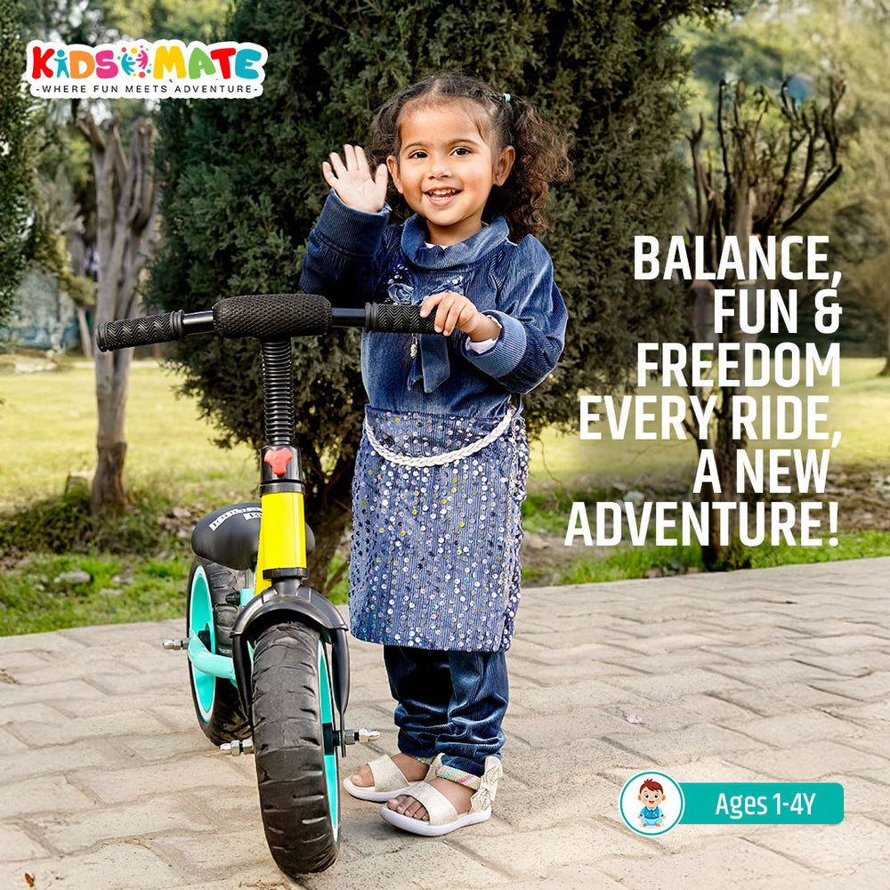 A cheerful child wearing a blue outfit smiles while standing next to a Kidsmate Glider Balance Bike. The bike features a sleek design with green wheels, set against a grassy background.
