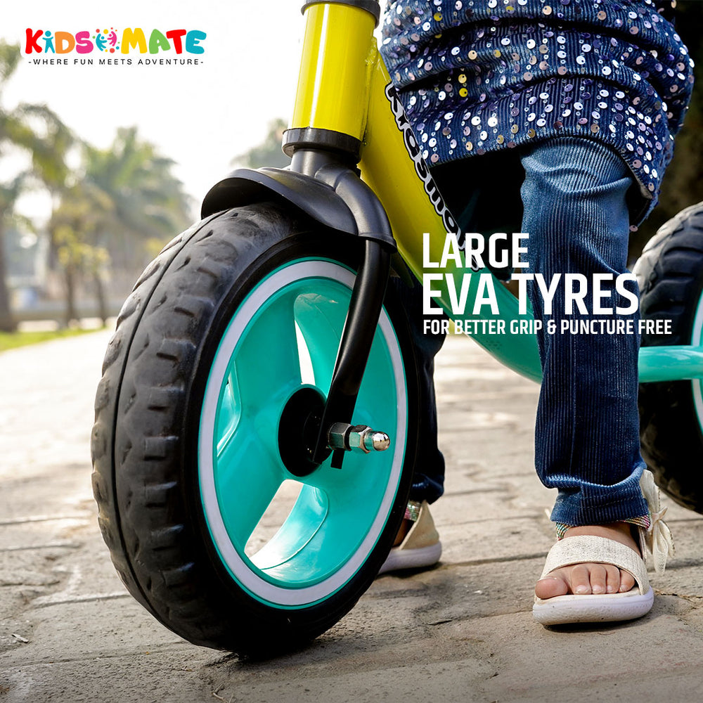A vibrant Kidsmate glider balance bike featuring large turquoise EVA tires. The bike is positioned on a pathway, with a child wearing denim and a polka dot top, ready to ride.