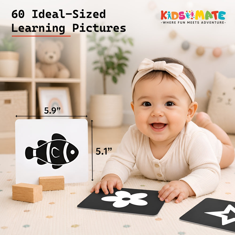 A happy baby with a headband sits on a soft surface, holding high contrast flash cards. One card features a fish design, while another shows a flower, promoting early learning.