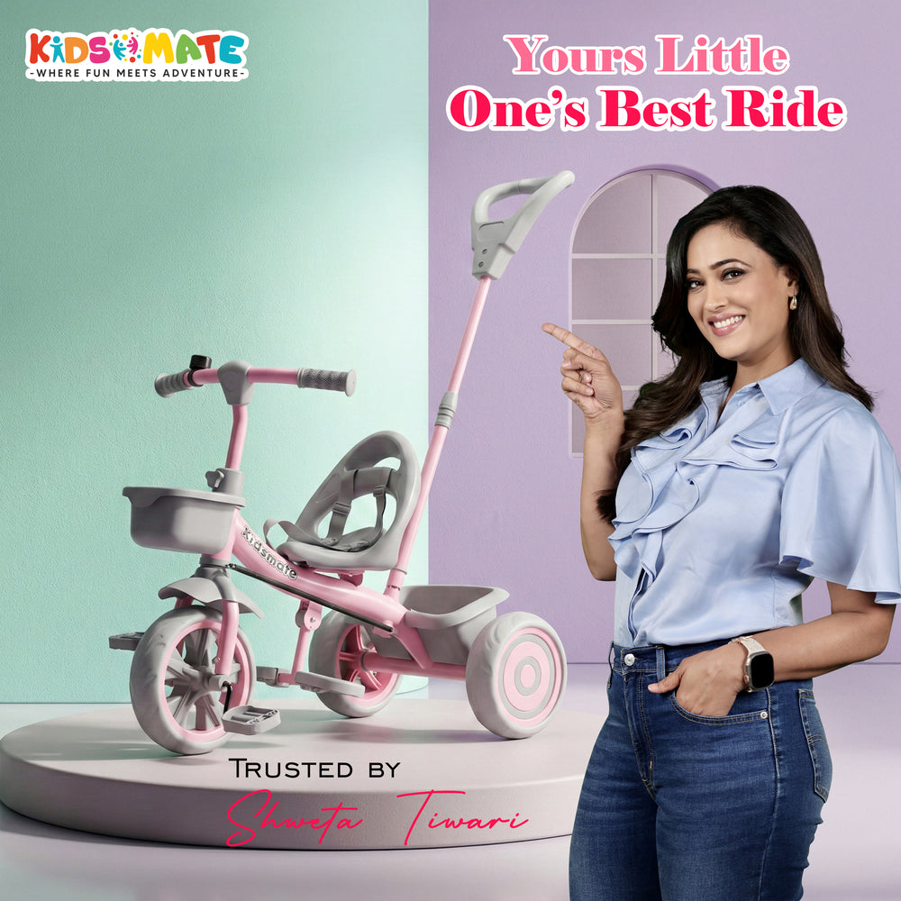 A colorful Kidsmate Junior Tricycle for kids, featuring a pink and white design with a parental control handle. A smiling woman stands beside it, promoting the product.