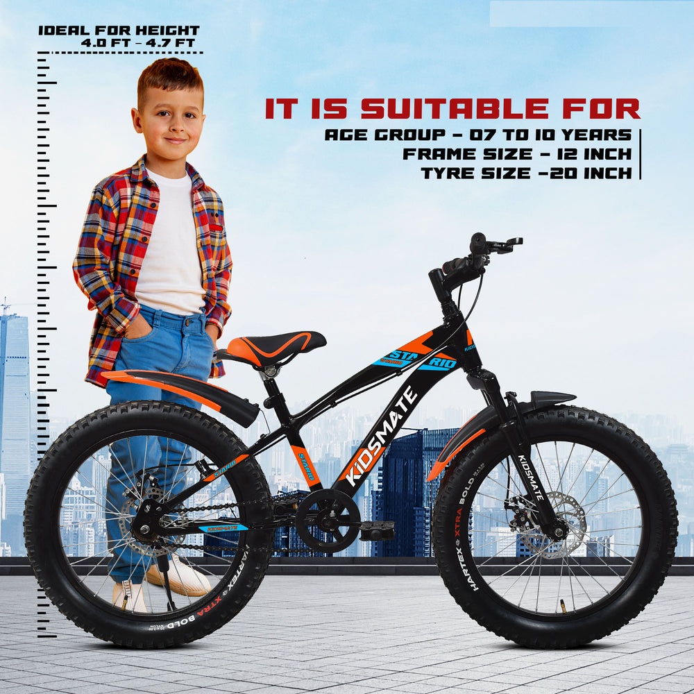 A vibrant kids bicycle with a black frame and orange accents, featuring large tires. A young boy stands beside the bike, smiling, wearing a plaid shirt and jeans. A height chart is visible in the background.