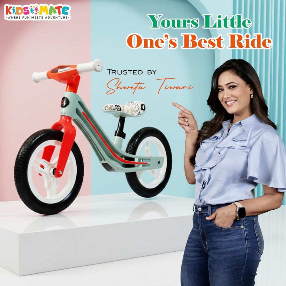 A colorful Kidsmate Zippy Balance Bike for kids, featuring a red and teal frame with white wheels. A smiling woman in a light blue shirt stands beside it, promoting the bike in a bright, cheerful setting.